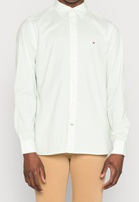 Camicia verde chiaro con bottoni, con piccoli pois bianchi, colletto a punta, maniche lunghe e un piccolo logo sul lato sinistro del petto.