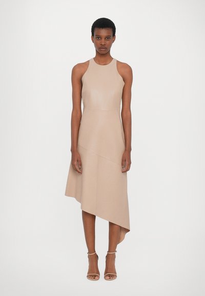 Robe sans manches beige avec un ourlet asymétrique et une texture lisse. Présente un corsage ajusté et est accompagnée de simples talons à lanières.