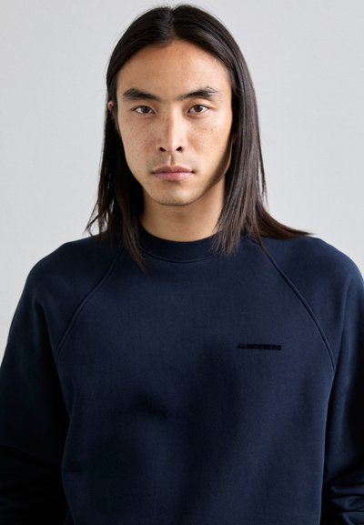 Sudadera azul marino con cuello redondo, mangas raglán y un acabado texturizado. Presenta un pequeño logo negro en el pecho.