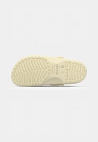 Semelle beige de chausson Crocs avec motif de bande de roulement texturé et marquages de taille 3/10 visibles, sur fond blanc uni.