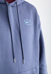 Blue hoodie made from soft fabric with a front kangaroo pocket, featuring a small light blue embroidered Nike logo and metal-tipped drawstrings.