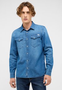 Sinine teksariidest särk pikkade varrukatega, ees nööpidega, kahe rinnataskuga ja vasakul taskul sildiga. Sile tekstuur ja klassikaline disain.