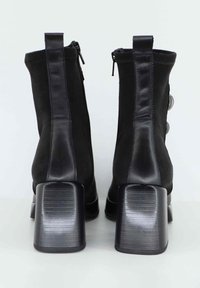 Stivaletti neri alla caviglia con una finitura in pelle e suede testurizzati, caratterizzati da un tacco a blocco rigido e striato e chiusura con zip sul retro.