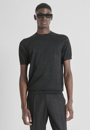 Crna pletena košulja kratkih rukava s diskretnim metalik sjajem, okruglim izrezom i pristajućim rubom, uparen s crnim hlačama suženog kroja. Glatka tekstura.