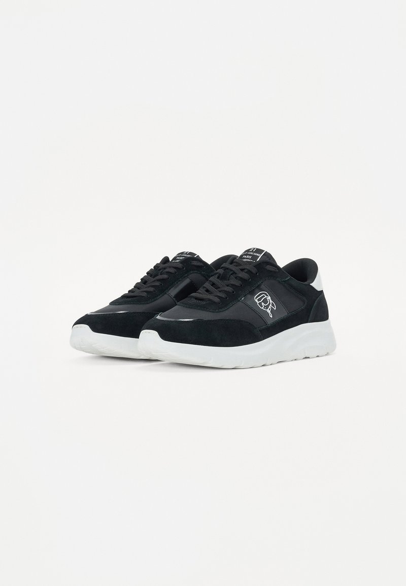 Des baskets noires avec une tige en cuir lisse et en daim, dotées d'une semelle en caoutchouc blanche et de détails de logo discrets sur le côté et la languette.
