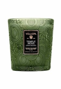 Grön koksvaxljushållare med texturerad yta som har cirkulära mönster. Svart etikett med texten "Temple Moss" och kollektionsdetaljer.