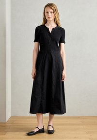 Black ribbed dress with short sleeves and a button-up neckline, featuring a flared skirt and solid texture. Paired with black flats.