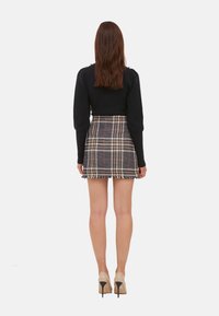 Un pull en tricot noir et une jupe mini à carreaux avec un ourlet à franges. La jupe présente des carreaux beiges, noirs et rouges. Des escarpins beiges viennent compléter le look.