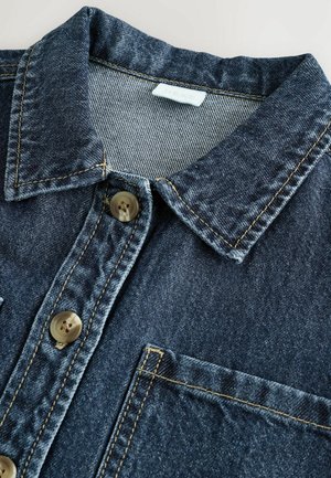 Denim shirt in een donkerblauwe kleur, met kraag, twee knopen en een voorzak. Zichtbare stitching in een contrasterende lichte kleur.