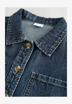 Džinsinė marškiniai, pasižymintys tamsiai mėlyna spalva, apykakle, dviem mygtukais ir priekinėmis kišenėmis. Matomas kontrastingos šviesios spalvos siuvinėjimas.