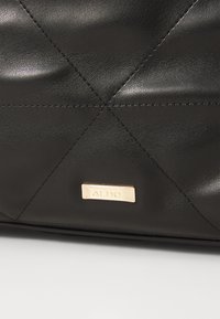 Sac en cuir noir avec un design matelassé, des coutures en diagonale et un accent en métal doré. Texture lisse avec une finition épurée.