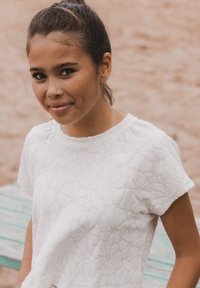 Witte gemarmerde shirt met een bloemenpatroon, korte mouwen en een ronde halslijn, gedragen door een persoon met een lichte achtergrond.