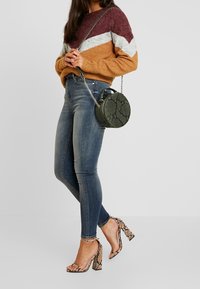 Suéter multicolorido con rayas en color burdeos, gris y naranja; jeans ajustados azules; bolso redondo verde con estampado de serpiente; sandalias de tacón alto con patrón de serpiente.