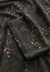 Nærbillede af gennemsigtigt sort stof med brun og beige leopardprint og foldede kanter med synlige syninger.