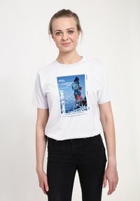 Biała bawełniana koszulka z niebieskim nadrukiem przedstawiającym górski krajobraz oraz tekst "SINCE 1981 DUNHAM MOUNTAINEERING."