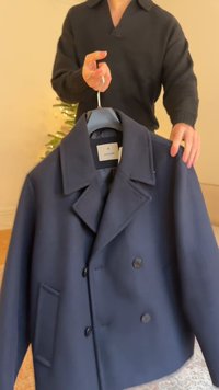 Soe sinise tooniga topeltkaravaniline mantel, millel on suured kraed ja küljetasku. Valmistatud siledast kangast, riputatud nagile, mida hoiab inimene.