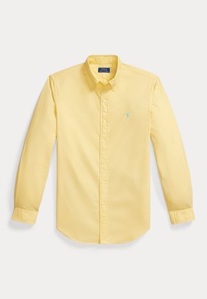Żółta koszula z długim rękawem, zapinana na guziki, z kołnierzykiem i jasno niebieskim haftowanym logo na lewej piersi, wyłożona na płasko na białym tle.