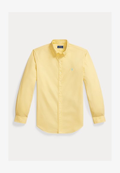 Chemise jaune à manches longues avec boutons et col, avec un logo brodé bleu clair sur la poitrine gauche, posée à plat sur un fond blanc.