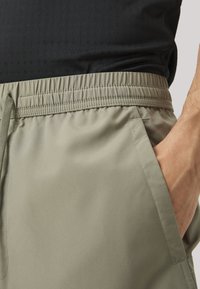 Pantaloni corti da uomo in khaki, realizzati in tessuto morbido, con vita elasticizzata e tasche. La vita è arricciata, offrendo comfort e flessibilità.
