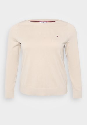 Pull beige à manches longues avec un col rond, fabriqué en matériau tricoté doux. Il présente un petit logo sur la poitrine et des poignets côtelés.
