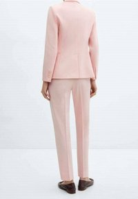 Costume rose clair sur mesure avec un blazer cintré et un pantalon à jambes droites, présentant des boutons simples et une texture de tissu lisse.
