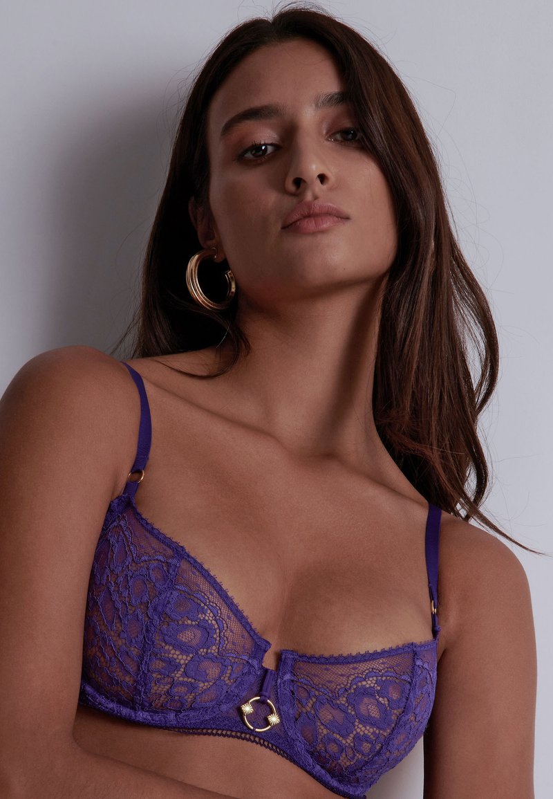 Soutien-gorge en dentelle violette avec de délicats motifs floraux, straps ajustables et un accent en métal doré au centre avant.