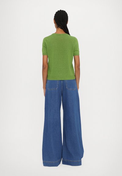 Grøn kortærmet top med ribbet tekstur, parret med brede blå denimjeans med to baglommer og kontrastsyninger.