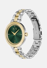 Ümmargune kell, millel on roheline kellanäidik, kuldse äärega ja hõbedast roostevabast terasest rihm, millel on vahelduvad kuldset värvi aktsendid ja pandla. 