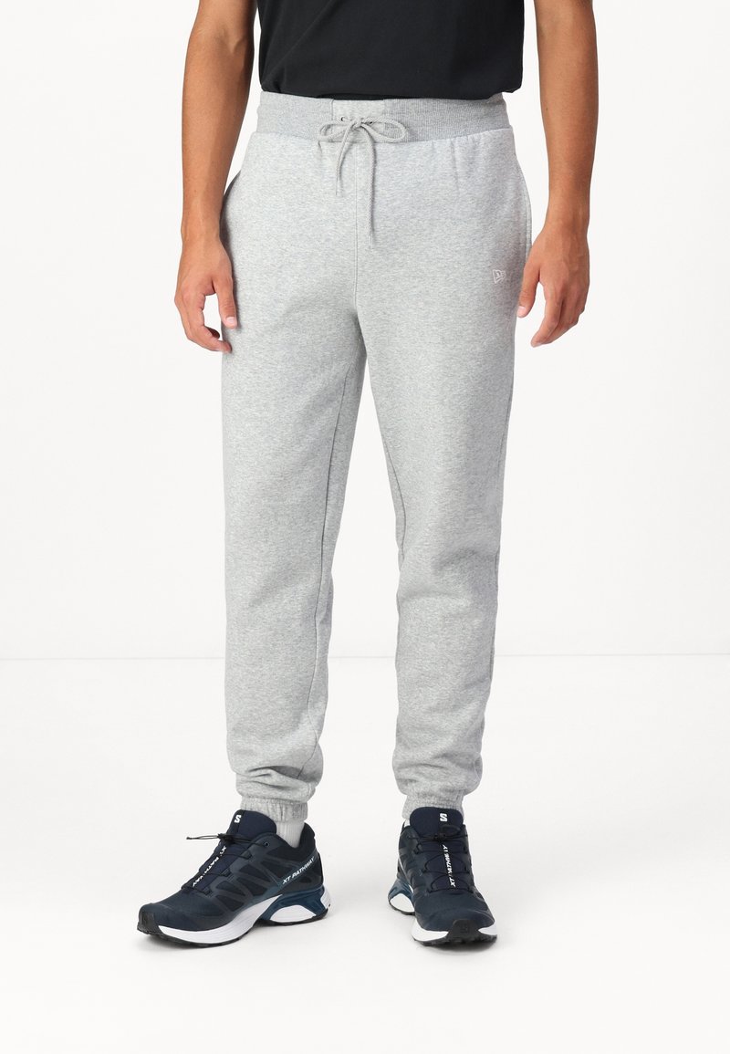 Gray cotton sweatpants with a drawstring waist, tapered legs, and side pockets, paired with black and blue athletic shoes.