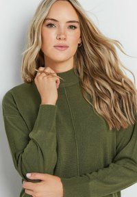 Maglione verde a collo alto in maglia con polsini a coste e una texture liscia. Presenta un sottile dettaglio in cucitura sul davanti.