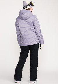Pufferjakke i lys lavendel med horisontal quilting, parret med sorte ski bukser og cremefarvede handsker. Uld beanie med logo bånd.