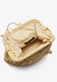 Woven straw handbag with a beige interior, gold chain strap, and a secure flap closure featuring a label inside.