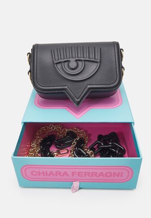 Musta nahkalaukku, jossa on kohokuvioitu silmäkuvio, avoimen sinisen ja vaaleanpunaisen Chiara Ferragnin laatikon päällä, jossa on kultaisia ja mustia ketjuja.