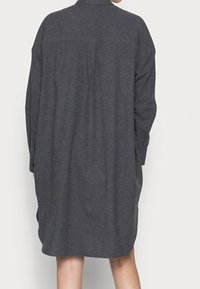 Długa, szara sukienka z długim rękawem, uszyta z miękkiego, teksturowanego materiału. Posiada zapinane na guziki z przodu, kołnierzyk oraz luźny krój z bocznymi kieszeniami.