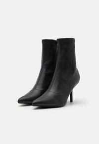 Botines de cuero negro con punta afilada y tacones altos de aguja. Cuentan con un zipper lateral y una textura suave, con detalles de costura.
