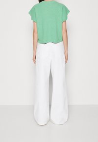 Krótki zielony sweter dzianinowy z rękawami typu cap, zestawiony z białymi spodniami o szerokich nogawkach, które mają dwie tylne kieszenie i gładką fakturę.