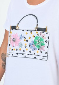 Witte T-shirt met een geprint handtasontwerp van roze en blauwe bloemen, gouden studs, zwarte stippen en een zwarte handgreep.