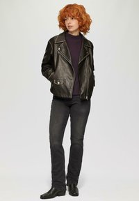 Schwarze Leder-Motorradjacke mit silbernen Beschlägen, Reißverschluss vorne und Seitentaschen, kombiniert mit dunklen Jeans und Knöchelstiefeln.
