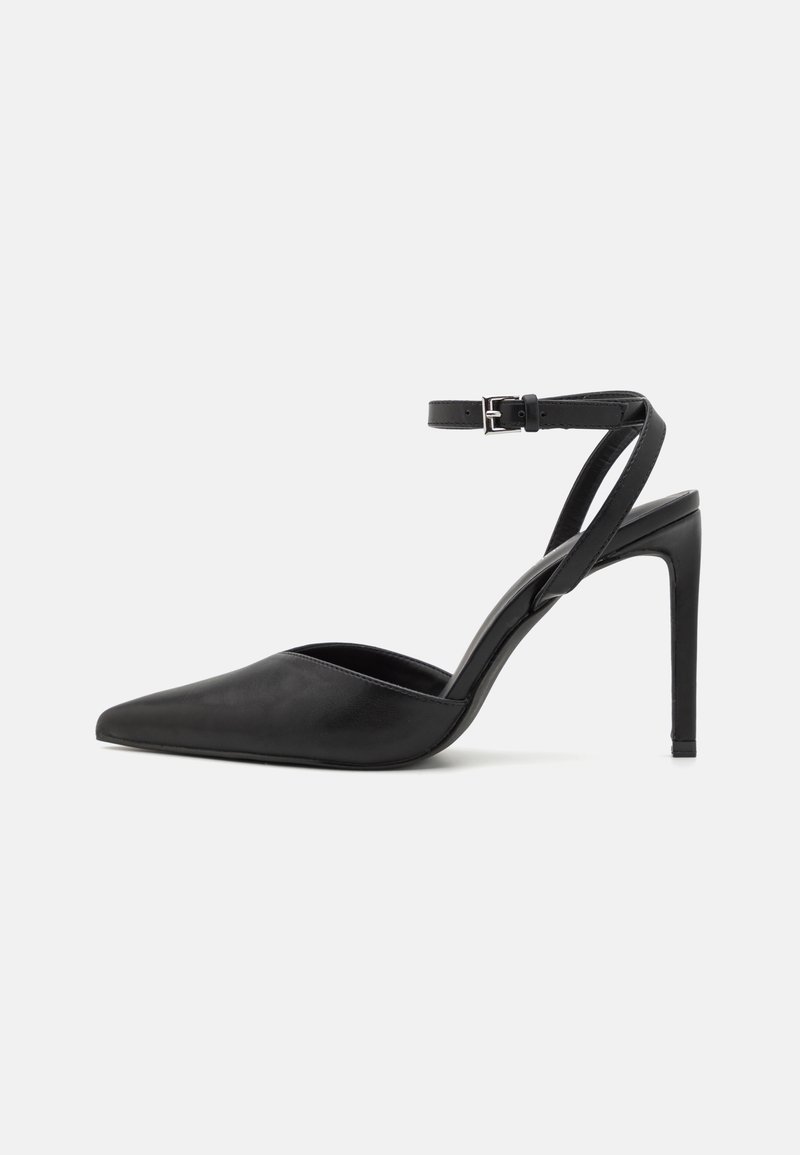 Escarpin noir à bout pointu avec talon stilettos, bride cheville et boucle argentée sur fond blanc.