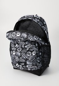Black backpack featuring white graphic prints of logos and patterns. Soft fabric, large main compartment, front pocket, and mesh side pockets.