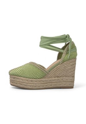 Espadrilla verde con tomaia in tessuto intrecciato, suola in juta intrecciata, dettagli testurizzati e lacci alla caviglia. Accentata da una leggera lucentezza.