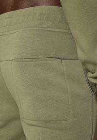 Olivegrønne joggebukser laget av myk bomullsblanding, med en sidelomme og elastisk midje med ribbedetaljer. Jevn tekstur, uformell design.
