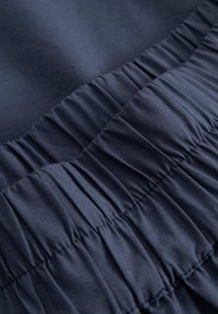 Zbliżenie ciemnoniebieskiej tkaniny z marszczoną elastyczną szwą, tworzącą równo rozmieszczone poziome fałdy.