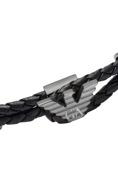 Bracelet en cuir noir tressé avec une fermeture argentée et un logo embossé présentant des ailes et les détails "GA". Texture lisse et design élégant.