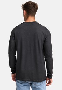 Schwarzes Langarmshirt mit Rundhalsausschnitt, geradem Saum und strukturiertem Stoff. Getragen mit hellblauen Jeans.