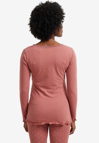 Long-sleeve top in dusty rose, featuring a scalloped neckline and a sleek fit. Soft fabric with a smooth texture, paired with dotted pants.