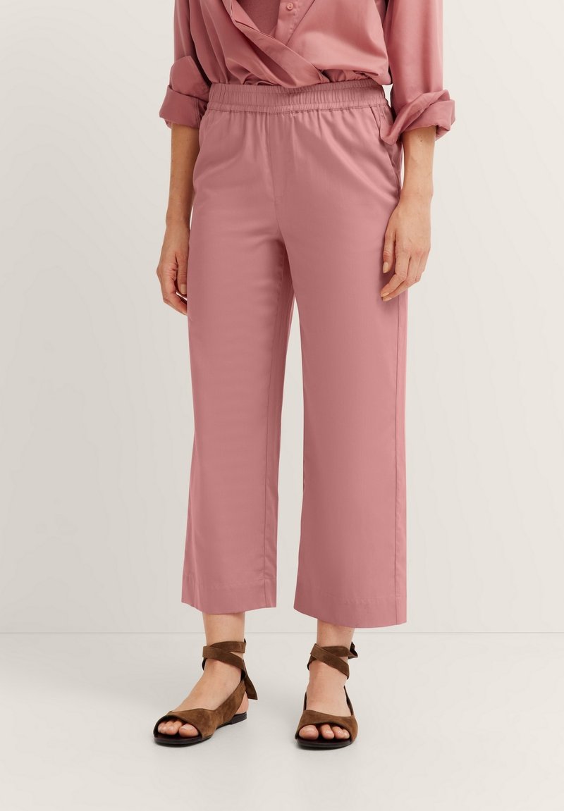 Helle rosa, elastische Cropped-Hosen mit geradem Schnitt, kombiniert mit braunen, geschnürten Sandalen und einer glatten Textur.