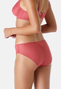 Set di lingerie in pizzo color corallo. Motivo floreale sul reggiseno e sul perizoma, con dettagli a margine ondulato. Tessuto liscio sul perizoma.