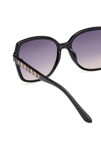 Gafas de sol negras de gran tamaño con lentes degradados. Presentan acentos decorativos en dorado en las patillas. Montura de plástico suave con un acabado brillante.