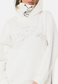 White oversized hoodie with a drawstring hood, featuring a shiny, studded "Legendary" design, a kangaroo pocket, and soft texture.